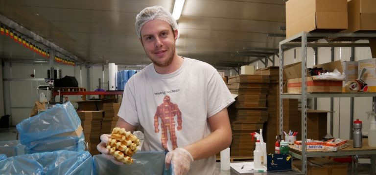 Man holds waffles while smiling at the camera