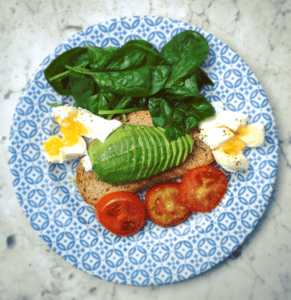 Aerial photo of a blue and white plate with bread, avocado, tomato, eggs and spinach